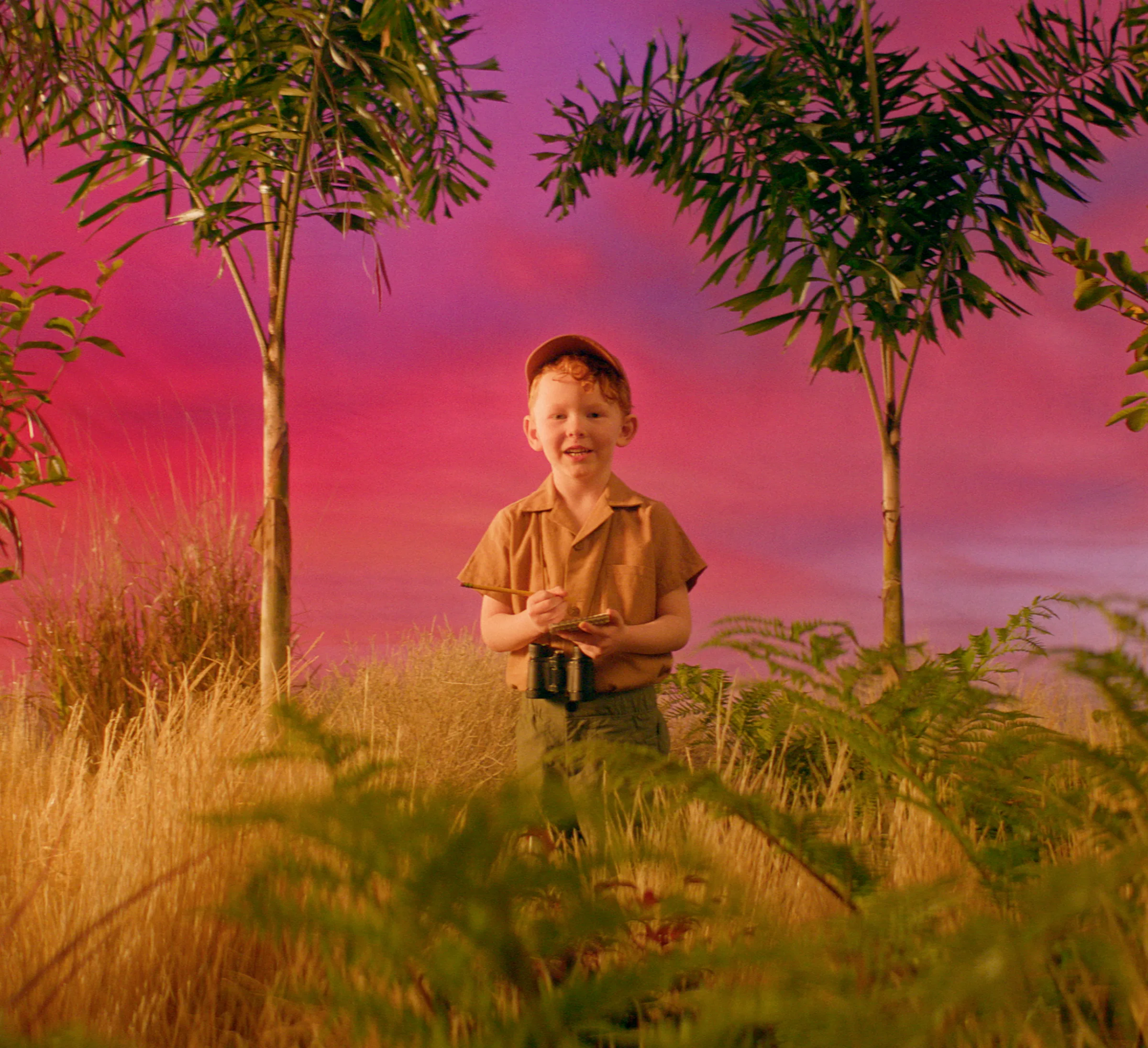 Young explorer framed by plants against a vivid pink sky